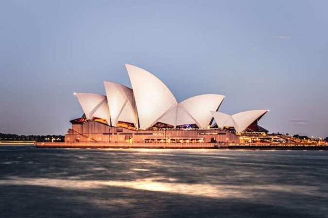 Opéra de Sydney illuminé au crépuscule au bord de l'eau avec le mot-clé monuments de Sydney.