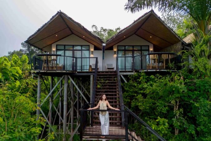 Une jeune femme posant sur les escaliers d'un éco-lodge sur pilotis entouré de végétation luxuriante lors d'un séjour à Khao Sok en Thaïlande.